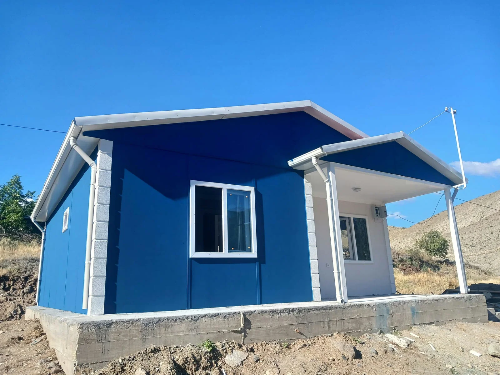 Tek katlı 1+1 yazlık prefabrik ev, mavi cephe ve beyaz sütunlu köşe verandası